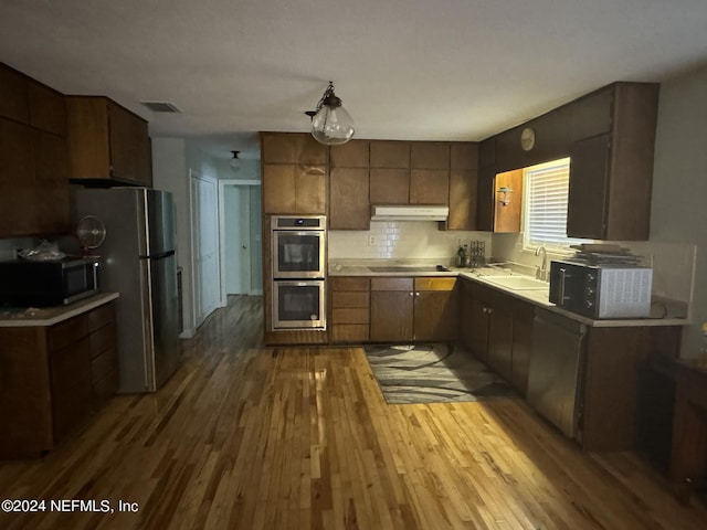 kitchen with decorative backsplash, sink, light wood-type flooring, and stainless steel appliances