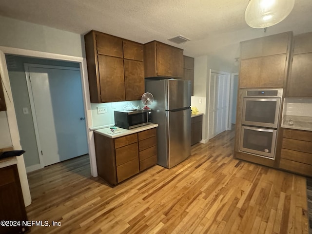 kitchen featuring light wood-type flooring, a textured ceiling, and appliances with stainless steel finishes