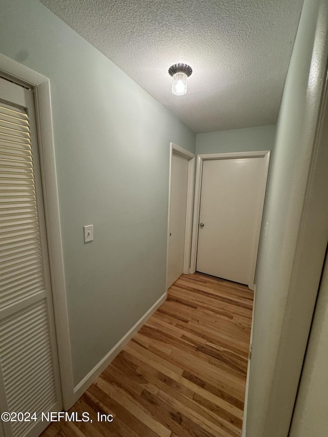 hallway with a textured ceiling and light hardwood / wood-style flooring