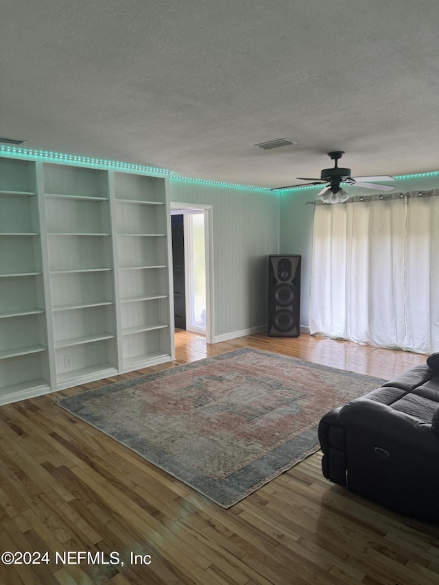 unfurnished living room with built in shelves, a textured ceiling, hardwood / wood-style flooring, and ceiling fan