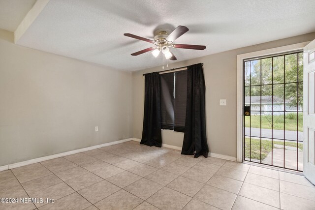 tiled empty room with ceiling fan and a textured ceiling