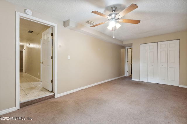 unfurnished bedroom featuring light carpet, a closet, ceiling fan, and a textured ceiling