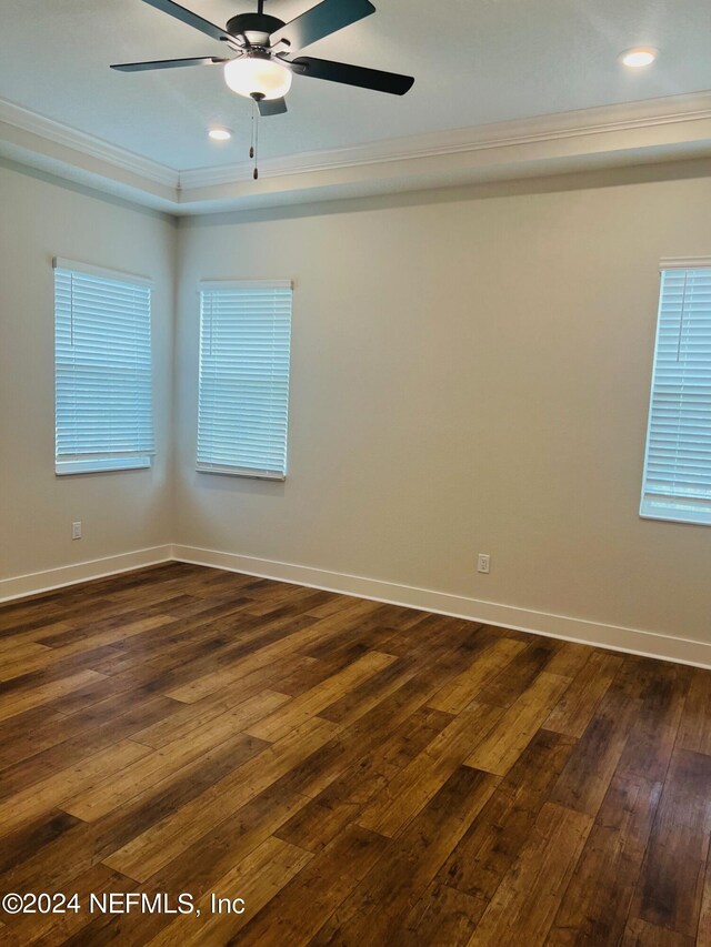 spare room with a tray ceiling, crown molding, and dark wood-type flooring