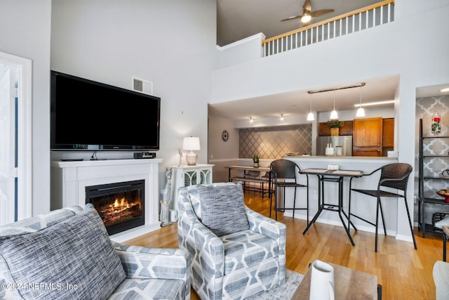 living room featuring a high ceiling, light wood-type flooring, and ceiling fan
