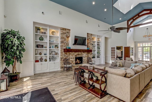 living room with a stone fireplace, built in shelves, a towering ceiling, and a skylight