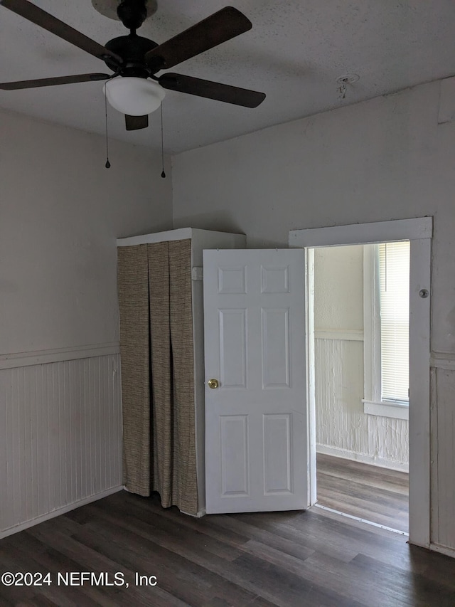 unfurnished bedroom featuring ceiling fan, dark wood-type flooring, and wood walls