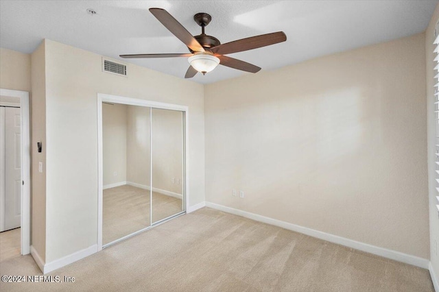 unfurnished bedroom with ceiling fan, light carpet, and a closet