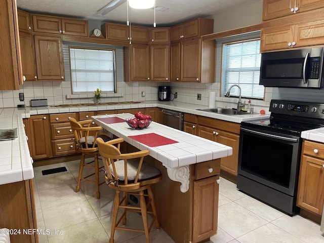 kitchen with appliances with stainless steel finishes, sink, backsplash, a center island, and tile counters