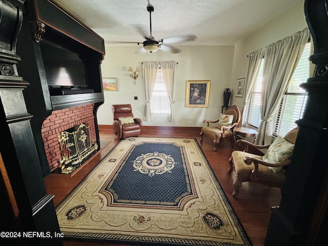 living room with a brick fireplace, wood-type flooring, and ceiling fan