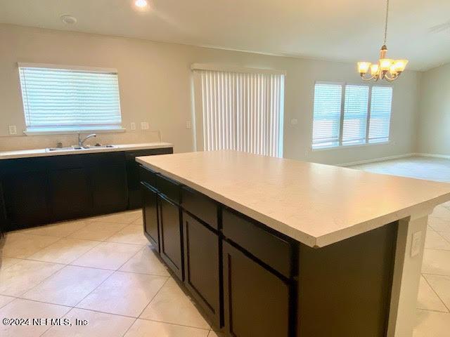 kitchen with sink, pendant lighting, light tile patterned floors, an inviting chandelier, and a kitchen island