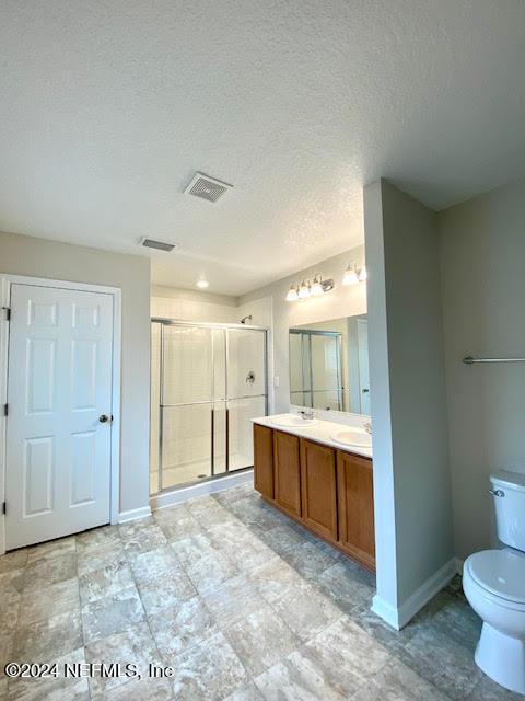 bathroom with a textured ceiling, vanity, an enclosed shower, and toilet