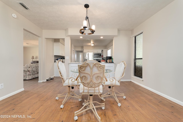 dining space with light hardwood / wood-style flooring, a chandelier, and a textured ceiling