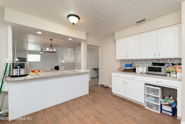 kitchen with hanging light fixtures, light hardwood / wood-style flooring, decorative backsplash, white cabinetry, and a chandelier