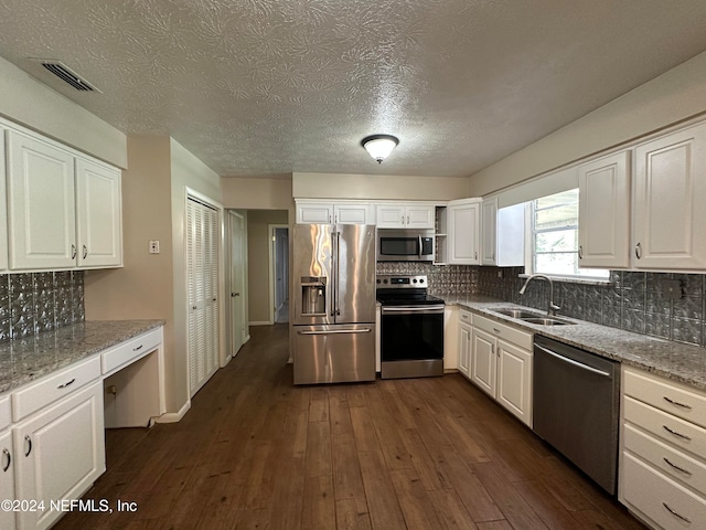 kitchen featuring appliances with stainless steel finishes, light stone counters, dark wood-type flooring, sink, and white cabinetry