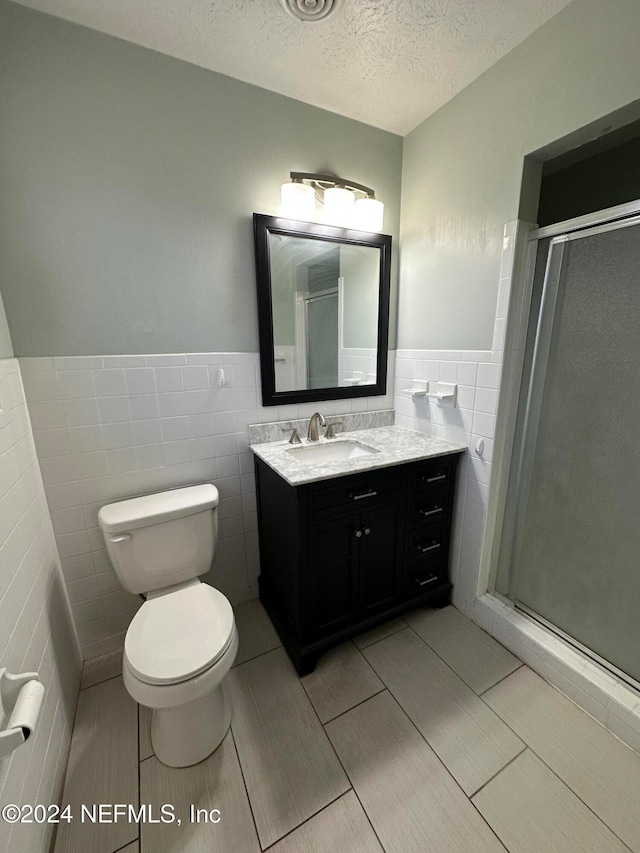 bathroom featuring vanity, a textured ceiling, tile walls, and an enclosed shower