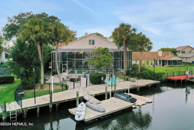 view of dock featuring fence private yard, a lanai, a water view, a lawn, and an outdoor pool