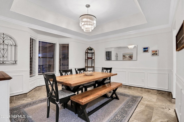 dining area with a tray ceiling, a decorative wall, an inviting chandelier, stone finish floor, and wainscoting