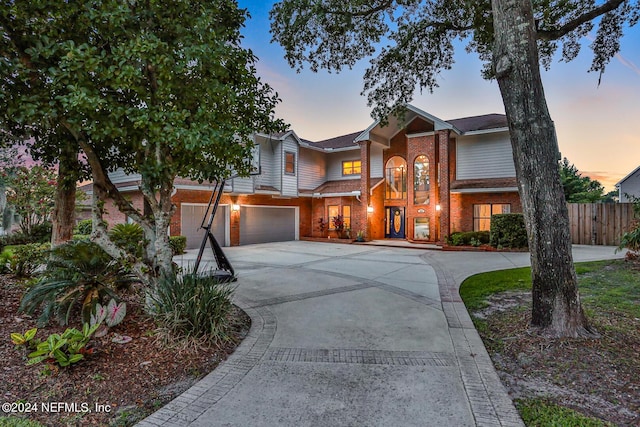 view of front of house featuring driveway, brick siding, an attached garage, and fence