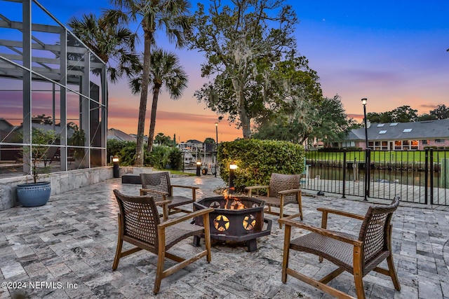 patio terrace at dusk featuring an outdoor fire pit, a lanai, and fence