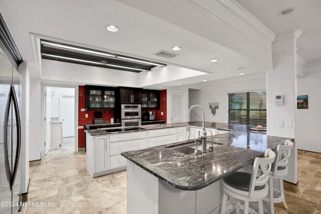 kitchen featuring stainless steel double oven, a sink, visible vents, stone finish floor, and a large island with sink