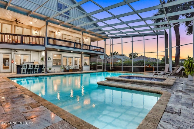 pool at dusk featuring an outdoor pool, glass enclosure, a patio area, and a jacuzzi