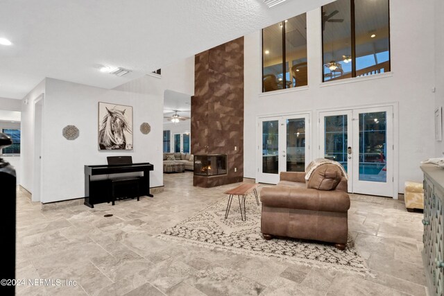 living area with a multi sided fireplace, visible vents, a ceiling fan, french doors, and stone finish floor