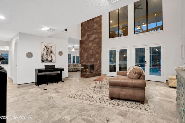 living area with ceiling fan, a multi sided fireplace, visible vents, french doors, and stone finish floor