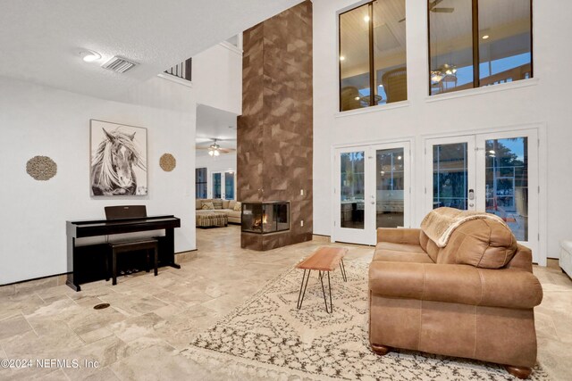 living area with french doors, visible vents, a high ceiling, a ceiling fan, and a multi sided fireplace