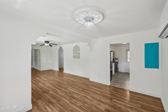 unfurnished living room with electric panel, baseboards, arched walkways, and wood finished floors