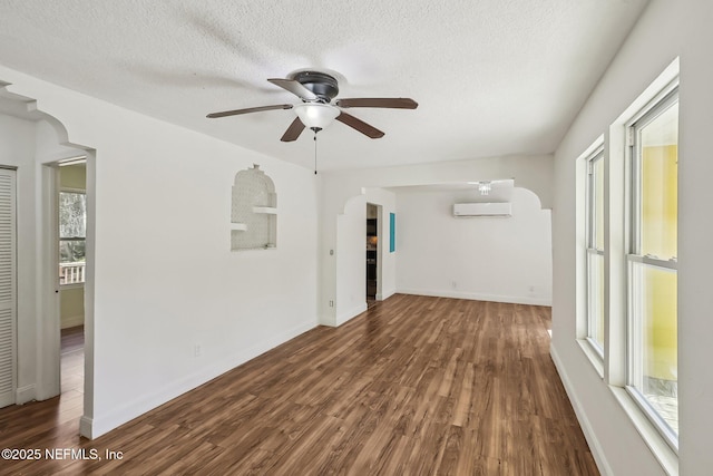 spare room featuring a wall mounted AC, a textured ceiling, wood finished floors, arched walkways, and baseboards