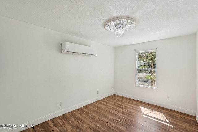 empty room with a wall mounted AC, a textured ceiling, wood finished floors, baseboards, and a chandelier