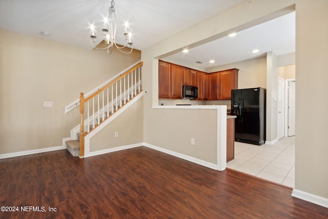 kitchen with pendant lighting, black appliances, a notable chandelier, and light hardwood / wood-style floors