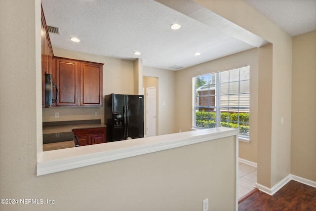 kitchen featuring black appliances, light wood-type flooring, kitchen peninsula, and a textured ceiling