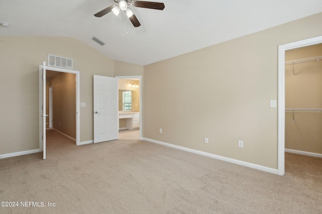 unfurnished bedroom with light carpet, a walk in closet, ceiling fan, a closet, and lofted ceiling