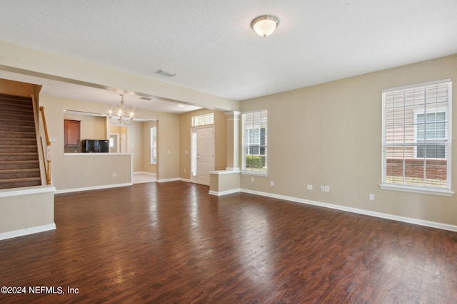 unfurnished living room with dark hardwood / wood-style floors, an inviting chandelier, and a wealth of natural light