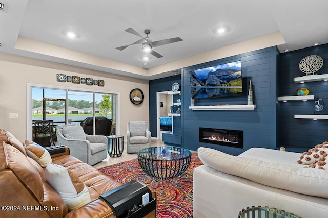 living room featuring ceiling fan, a large fireplace, and a raised ceiling