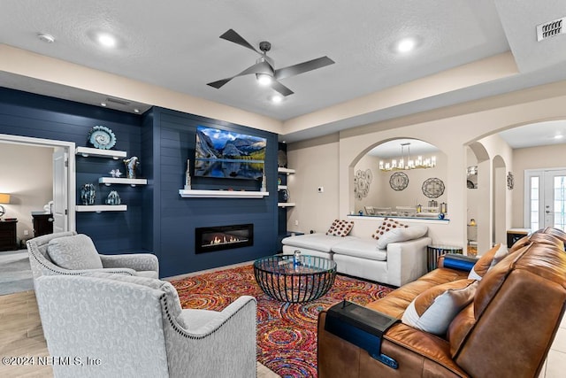 living room with a fireplace, ceiling fan with notable chandelier, a tray ceiling, and built in features