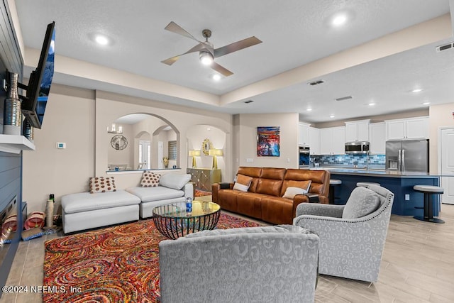 living room with a fireplace, light wood-type flooring, ceiling fan with notable chandelier, and sink