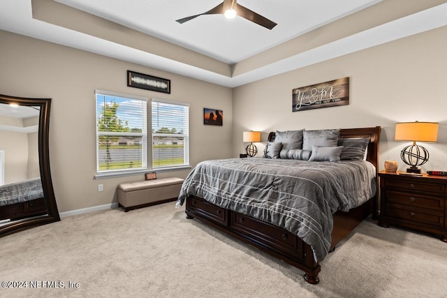 carpeted bedroom featuring a tray ceiling and ceiling fan