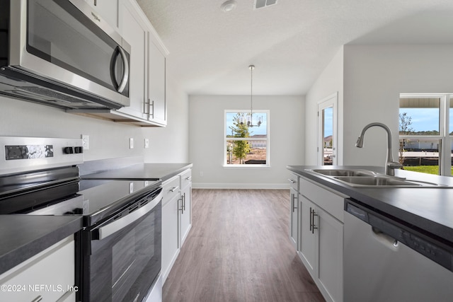 kitchen with appliances with stainless steel finishes, sink, a notable chandelier, white cabinets, and hanging light fixtures