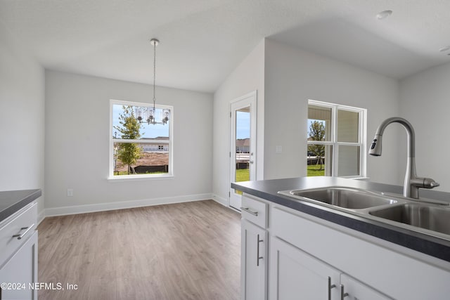 kitchen with pendant lighting, white cabinets, sink, a notable chandelier, and light hardwood / wood-style floors