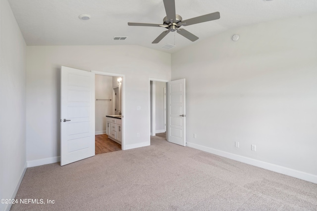 unfurnished bedroom with ceiling fan, light colored carpet, ensuite bathroom, and vaulted ceiling