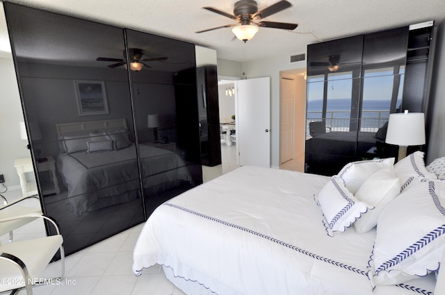 bedroom with a textured ceiling, access to outside, ceiling fan, a water view, and light tile patterned flooring