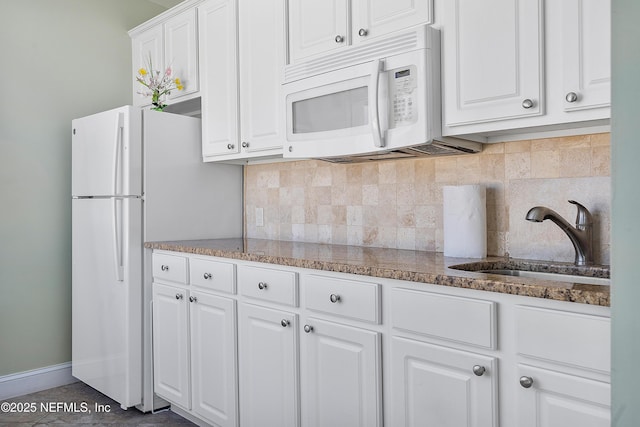 kitchen with white appliances, stone counters, white cabinets, sink, and decorative backsplash