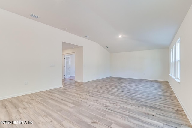 spare room featuring visible vents, baseboards, light wood-style floors, and vaulted ceiling