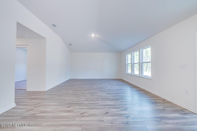 empty room with visible vents, light wood-type flooring, baseboards, and vaulted ceiling