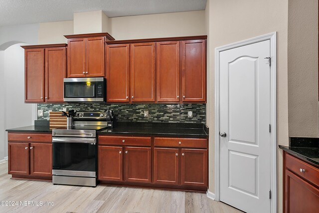 kitchen featuring backsplash, dark stone counters, light hardwood / wood-style floors, and appliances with stainless steel finishes