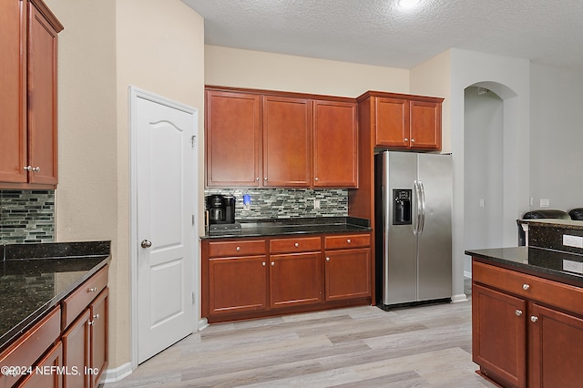 kitchen with light hardwood / wood-style floors, stainless steel fridge with ice dispenser, a textured ceiling, and tasteful backsplash