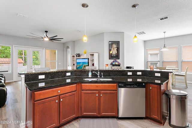 kitchen featuring a center island with sink, sink, hanging light fixtures, stainless steel dishwasher, and dark stone countertops