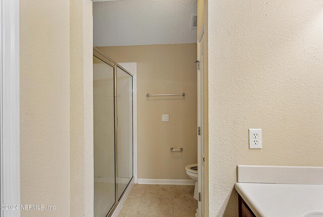 bathroom featuring tile patterned flooring, a textured ceiling, toilet, vanity, and a shower with shower door